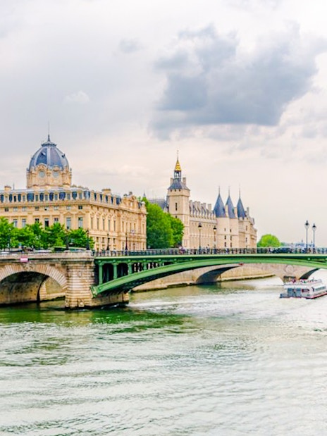 Seine River cruise boat passing under a bridge with historic Parisian architecture in the background.