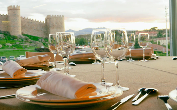 Dining table set with glassware, overlooking the historic Walls of Ávila, Spain.