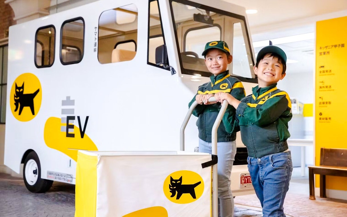 Children in delivery uniforms with electric vehicle at KidZania Osaka Koshien.