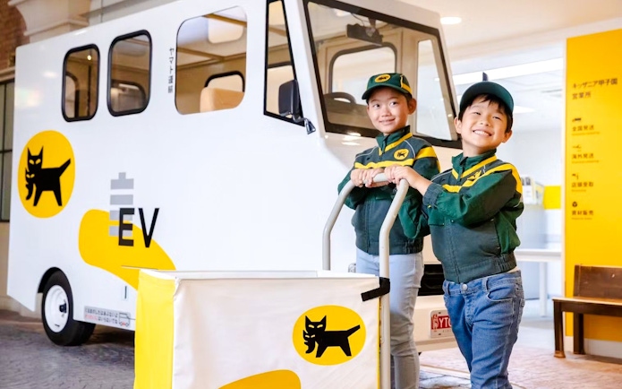 Children in delivery uniforms with electric vehicle at KidZania Osaka Koshien.