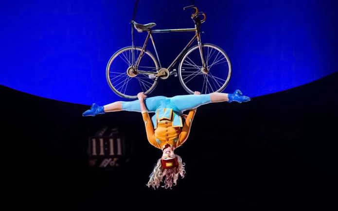 Performer hanging upside down with a bicycle at Cirque du Soleil: Kurios in Vienna.