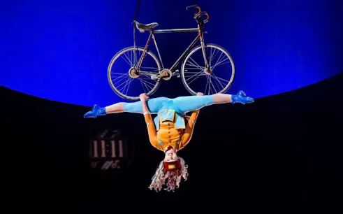Performer hanging upside down with a bicycle at Cirque du Soleil: Kurios in Vienna.