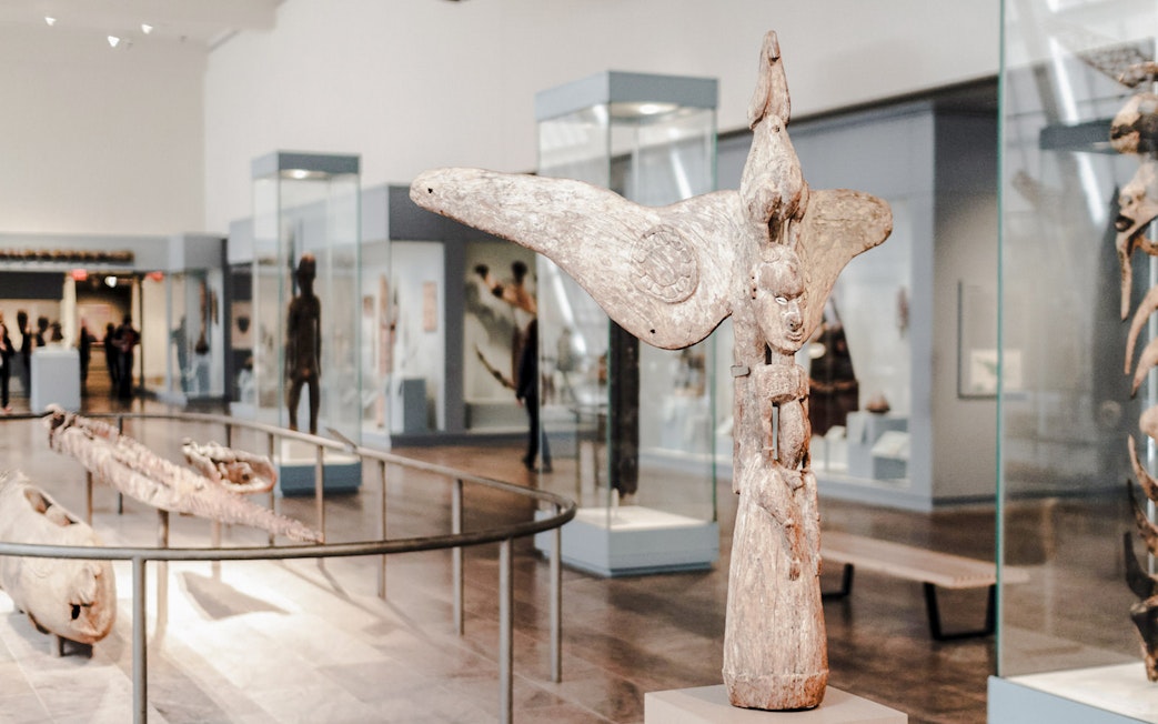 Wooden sculptures and artifacts in glass cases at the Metropolitan Museum of Art gallery.