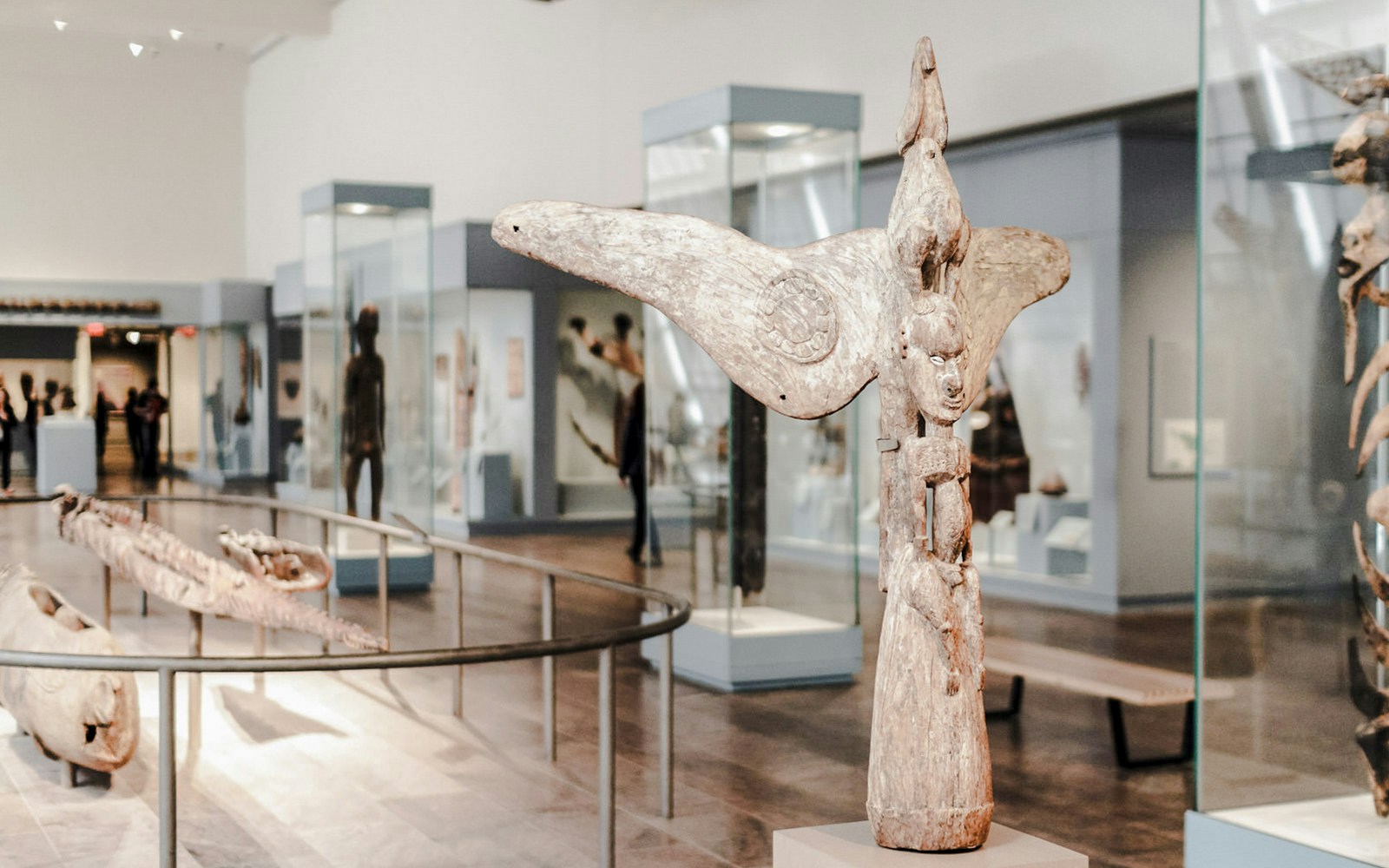 Metropolitan Museum of Art gallery with wooden sculptures and artifacts in glass cases and on pedestals.