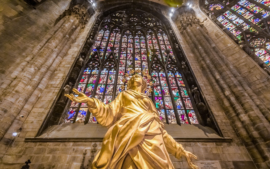 Golden statue and stained glass inside Duomo Cathedral, Milan.