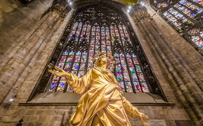 Golden statue and stained glass inside Duomo Cathedral, Milan.