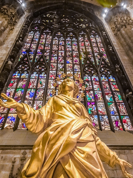 Golden statue and stained glass inside Duomo Cathedral, Milan.