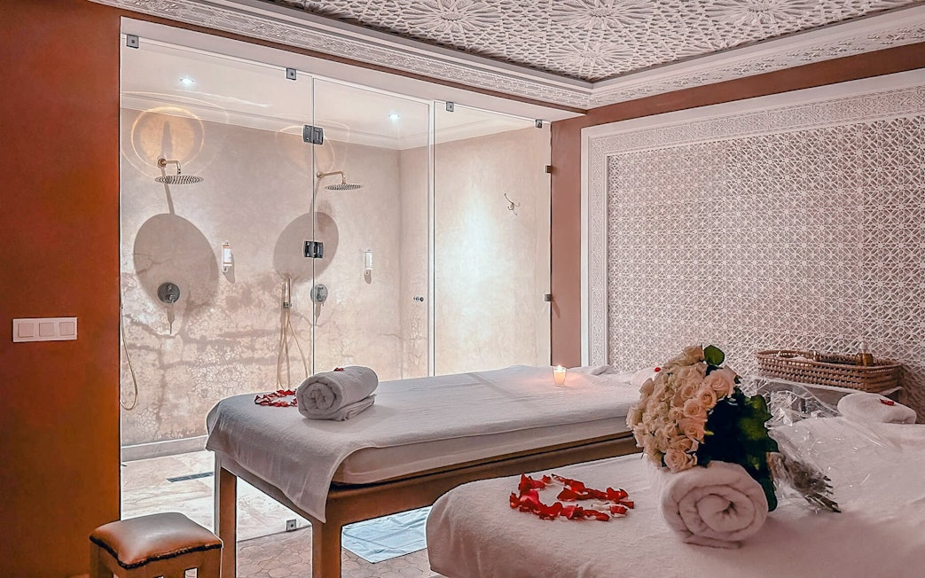 Luxury steam hammam spa room with massage tables, rose petals, and glass shower.