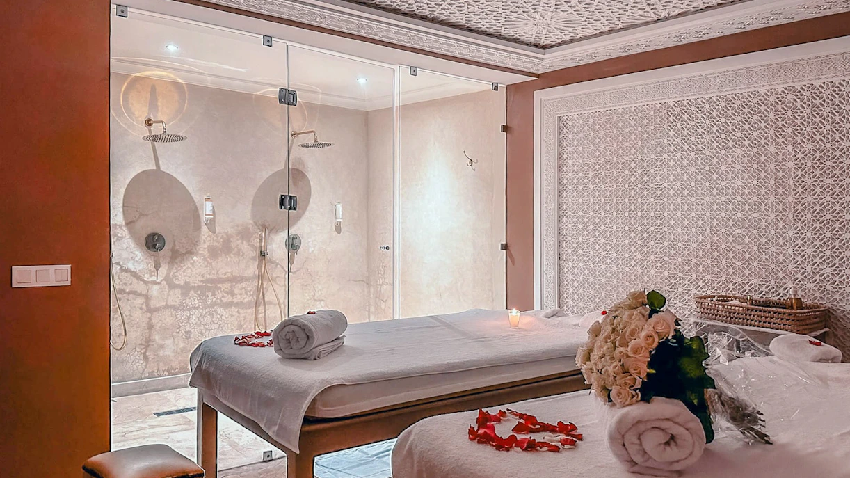 Luxury steam hammam spa room with massage tables, rose petals, and glass shower.