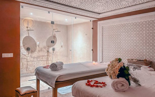 Luxury steam hammam spa room with massage tables, rose petals, and glass shower.