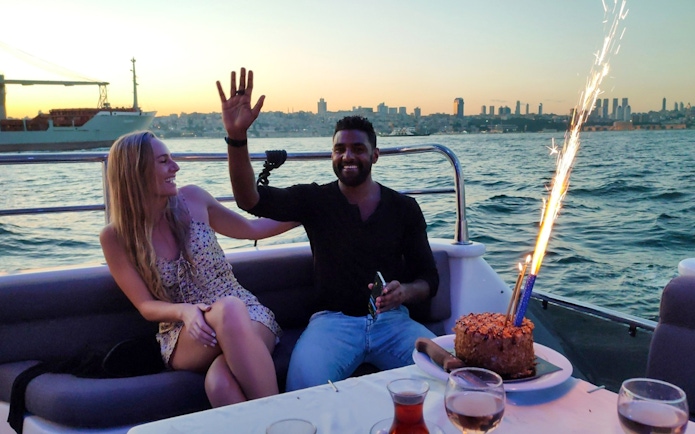 Couple enjoying sunset on Istanbul Bosphorus boat cruise with cake and sparklers.