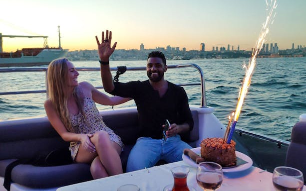 Couple enjoying sunset on Istanbul Bosphorus boat cruise with cake and sparklers.