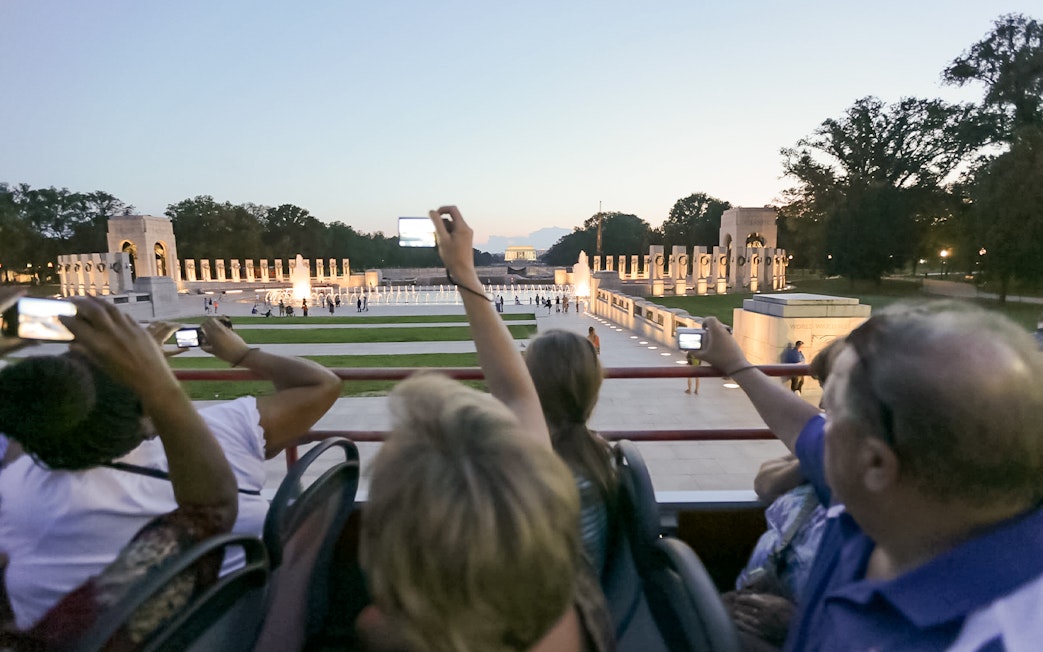 Tourists on a night bus tour photographing the illuminated World War II Memorial in Washington, D.C.