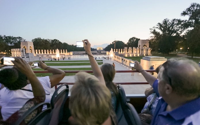 Tourists on a night bus tour photographing the illuminated World War II Memorial in Washington, D.C.