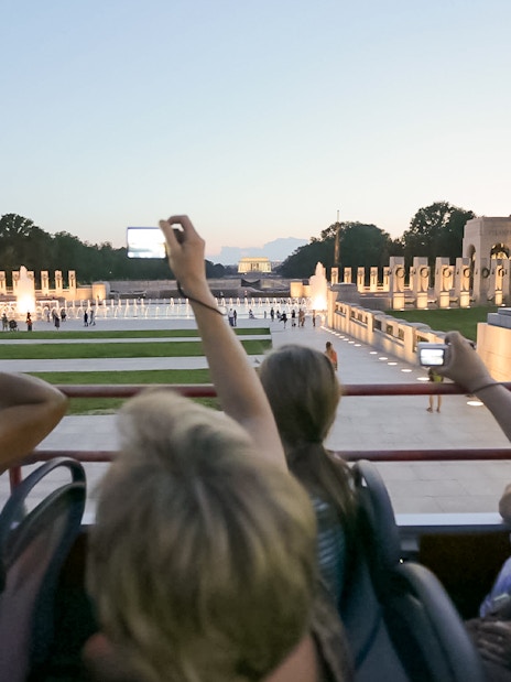 Tourists on a night bus tour photographing the illuminated World War II Memorial in Washington, D.C.