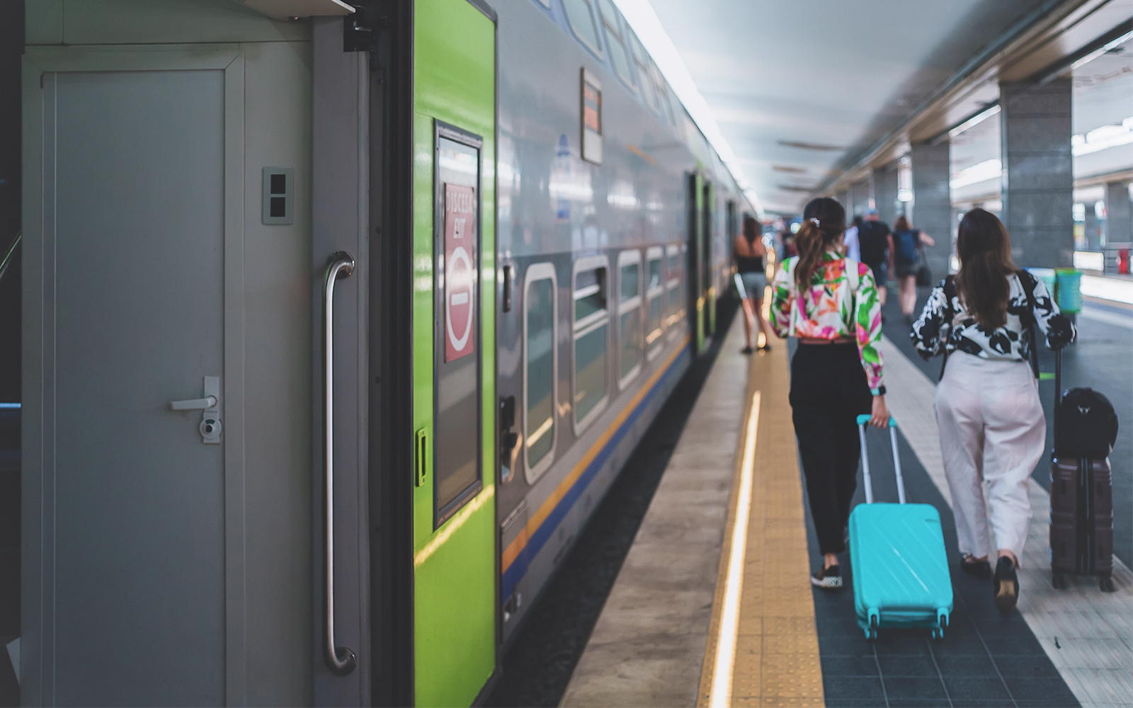 Passengers walking along Naples metro platform with train in view.