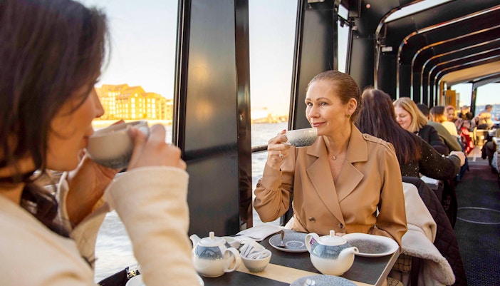 Afternoon tea on a Thames River cruise with people enjoying drinks and views of London.