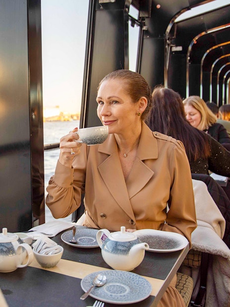 Afternoon tea on a Thames River cruise with people enjoying drinks and views of London.