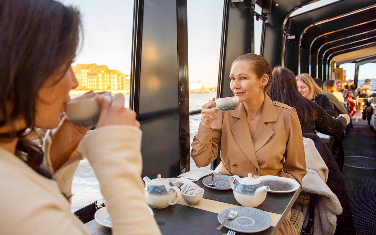 Afternoon tea on a Thames River cruise with people enjoying drinks and views of London.