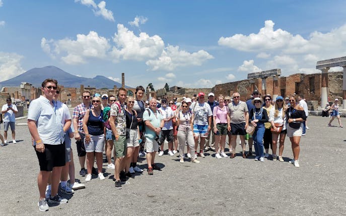 Group of tourists at Pompeii ruins with Mount Vesuvius in the background.