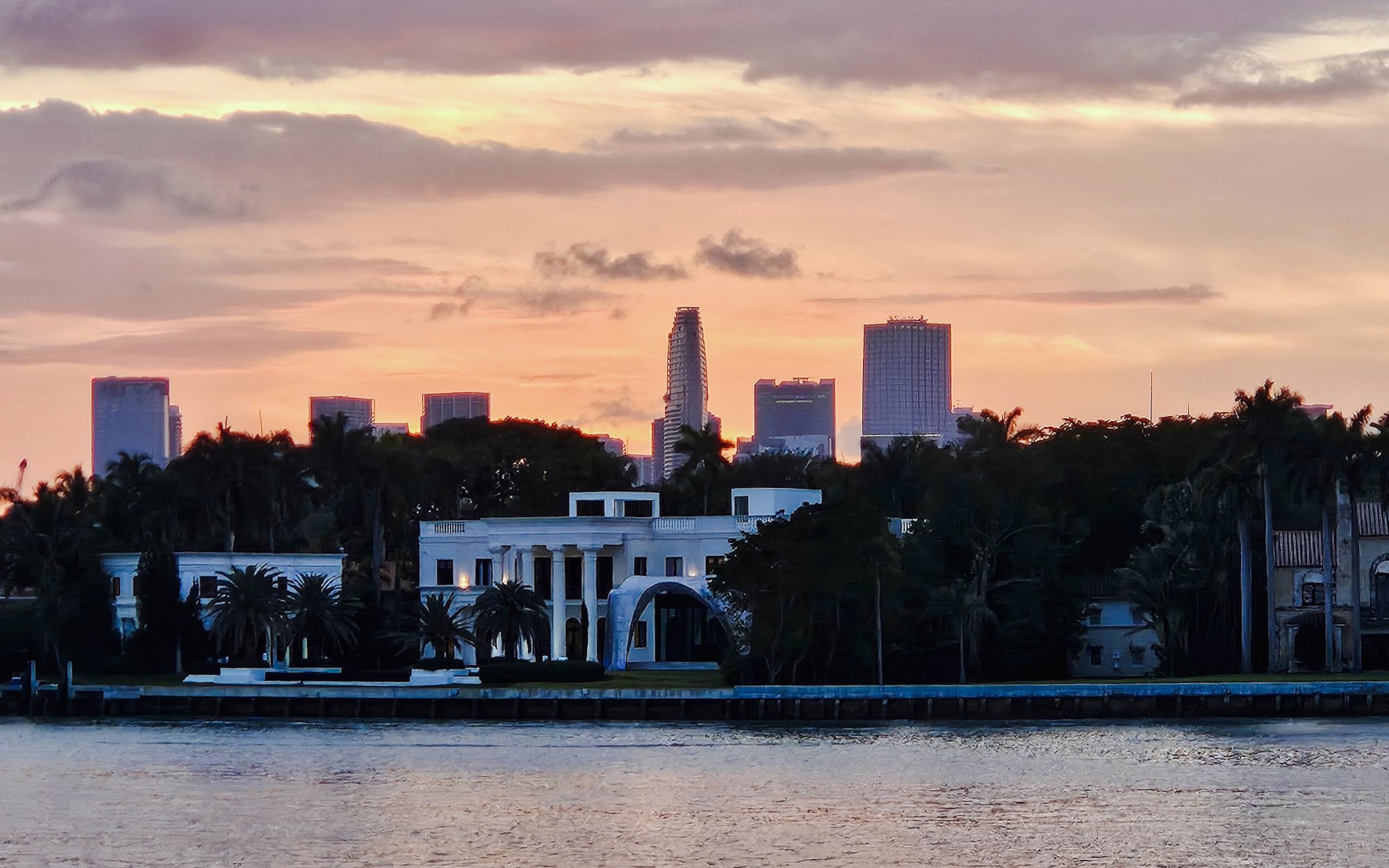 Miami skyline at sunset viewed from a cruise, with palm trees and waterfront buildings.