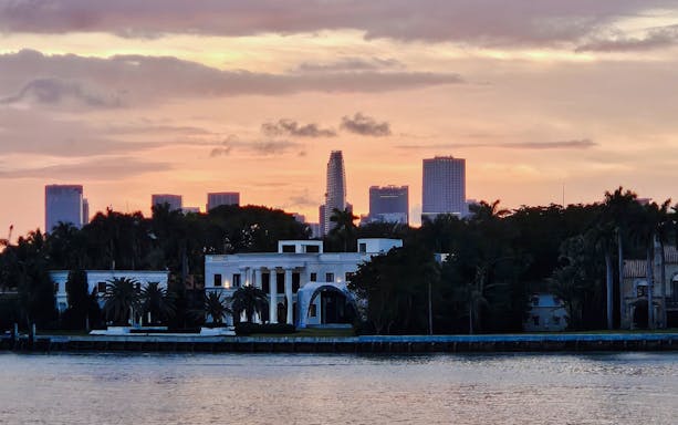 Miami skyline at sunset viewed from a cruise, with palm trees and waterfront buildings.