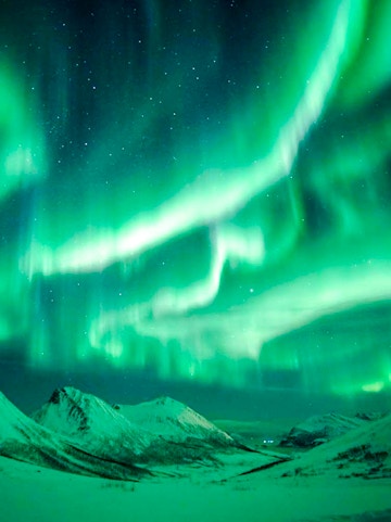 Northern Lights illuminating snowy mountains near Tromso, Norway.