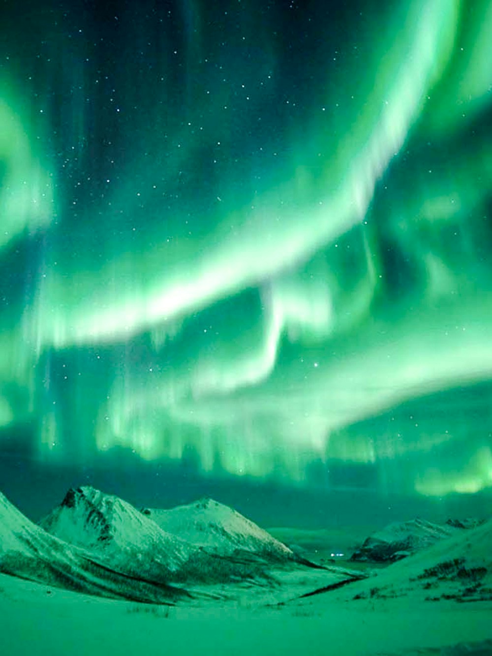 Northern Lights illuminating snowy mountains near Tromso, Norway.