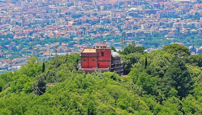 Vesuvius Observatory surrounded by lush greenery with cityscape in the background.