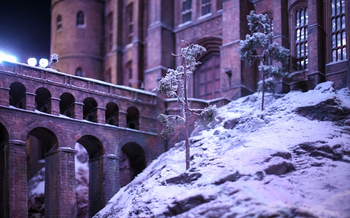 Snow-covered Hogwarts castle with bridge during Christmas season.