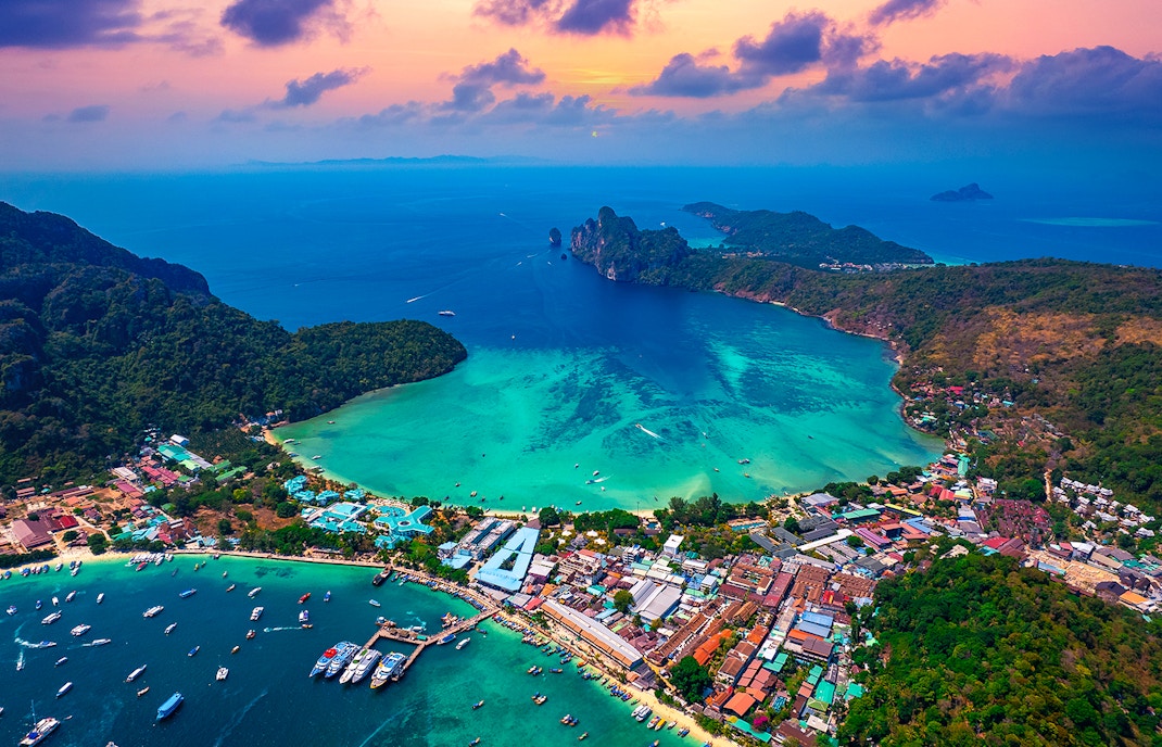 Drone view of Phi Phi Islands at sunset, showcasing vibrant skies and lush landscapes, Thailand.
