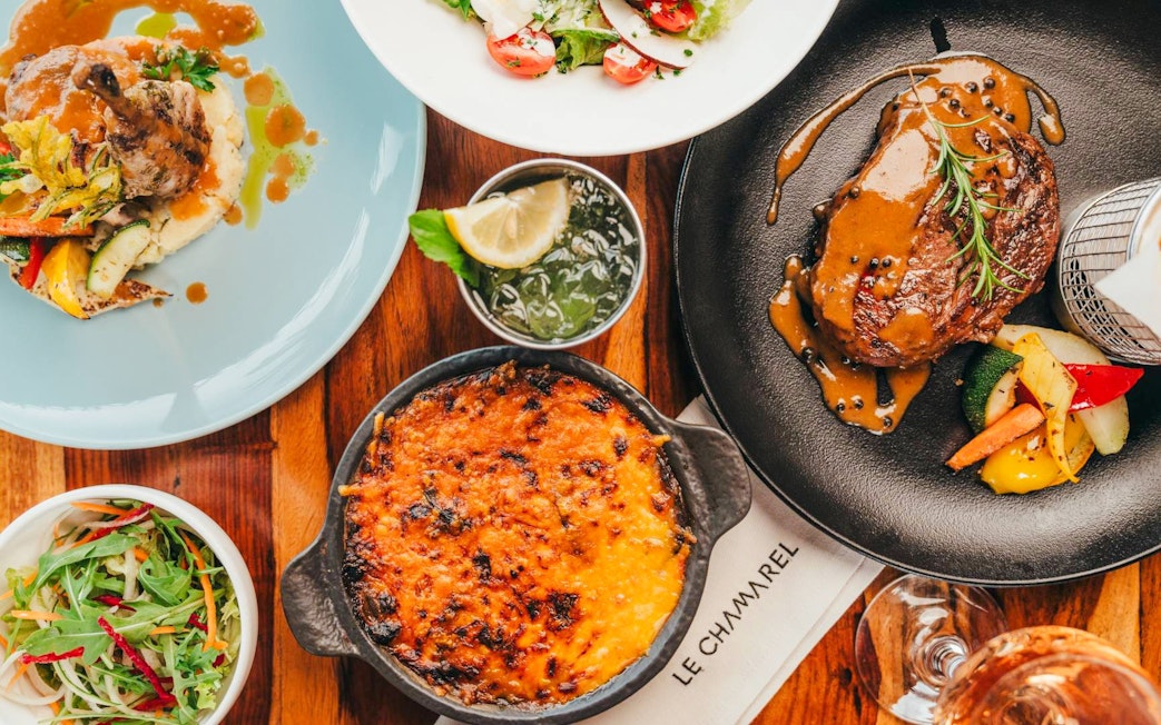 Assorted dishes at Coloured Earth in Chamarel, Mauritius, featuring steak, salad, and gratin.