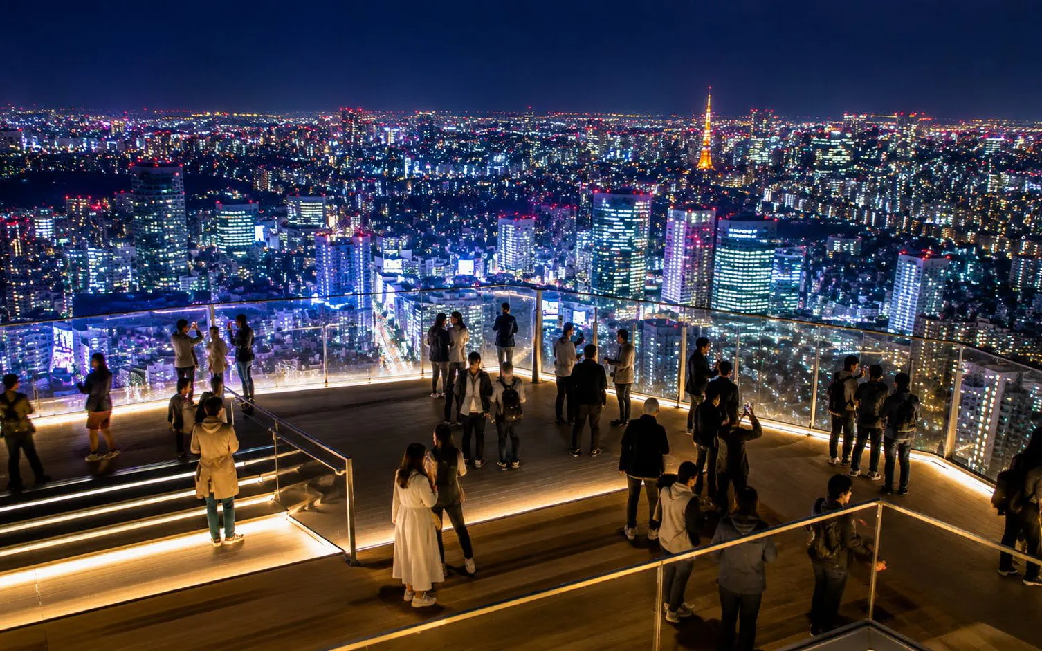 Visitors enjoying Tokyo's night skyline from Shibuya Sky observation deck.