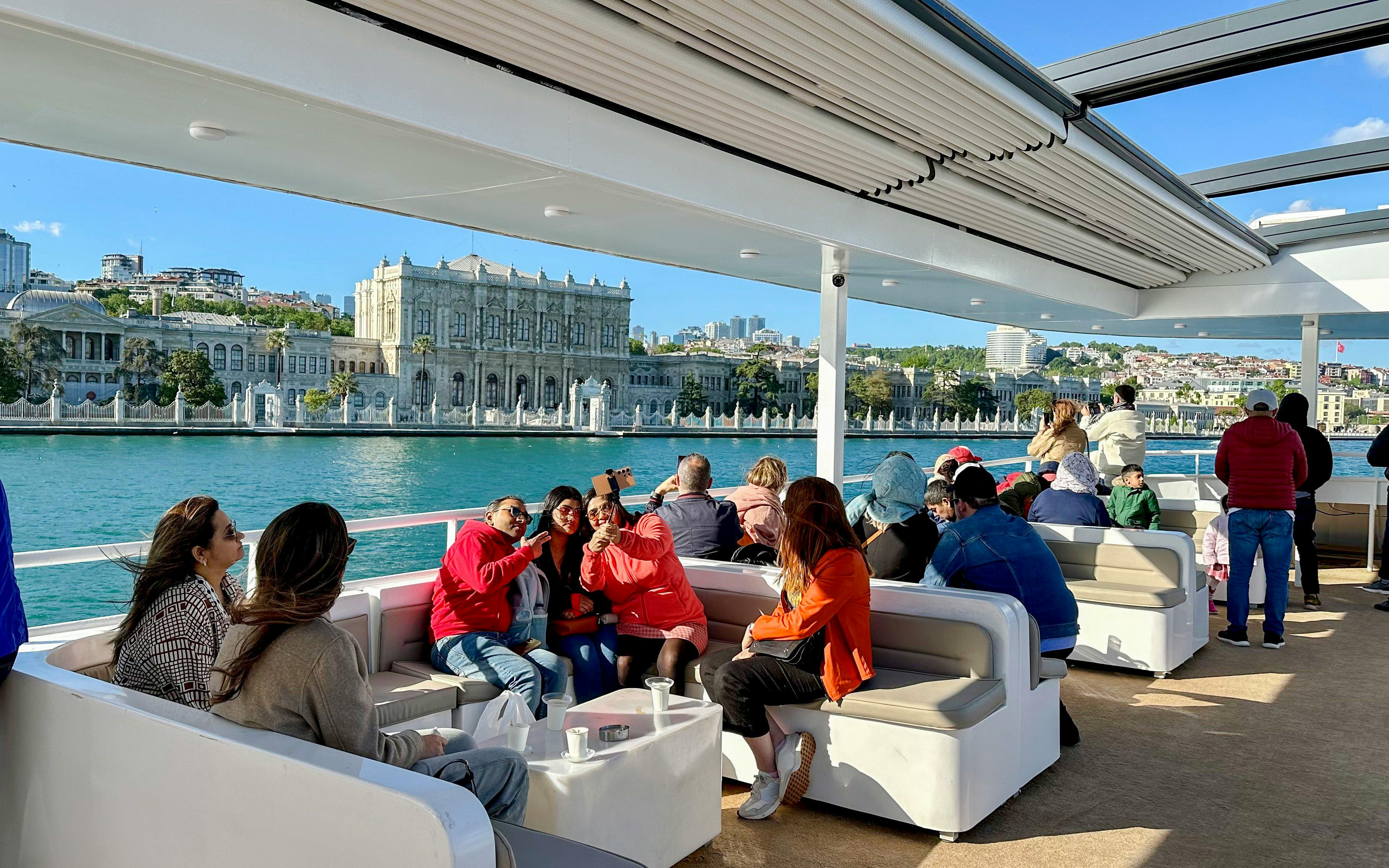 Guests enjoying a Bosphorus cruise with Dolmabahçe Palace in the background.