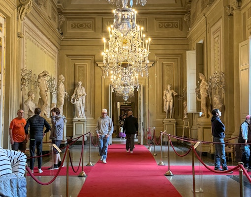 Visitors exploring statues and chandeliers in the Palatine Gallery, Pitti Palace, Florence.