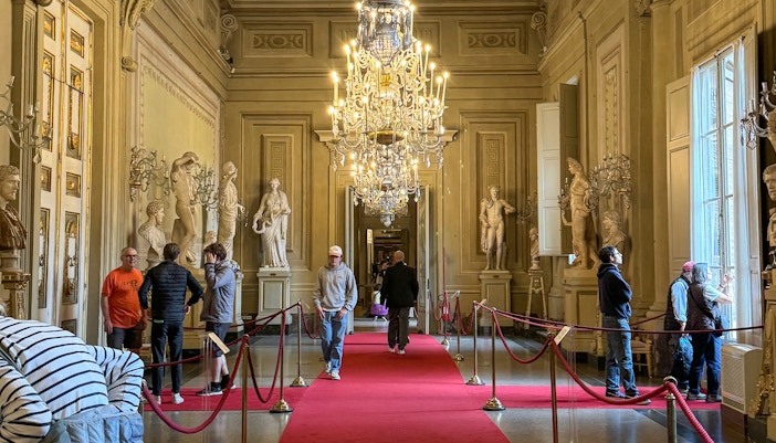 Visitors exploring statues and chandeliers in the Palatine Gallery, Pitti Palace, Florence.