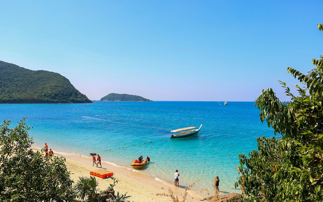 Tourists on a sandy beach with a boat at Nemo Island, clear blue water, Thailand.