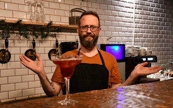 Local host in Icelandic restaurant with cocktail on bar counter.