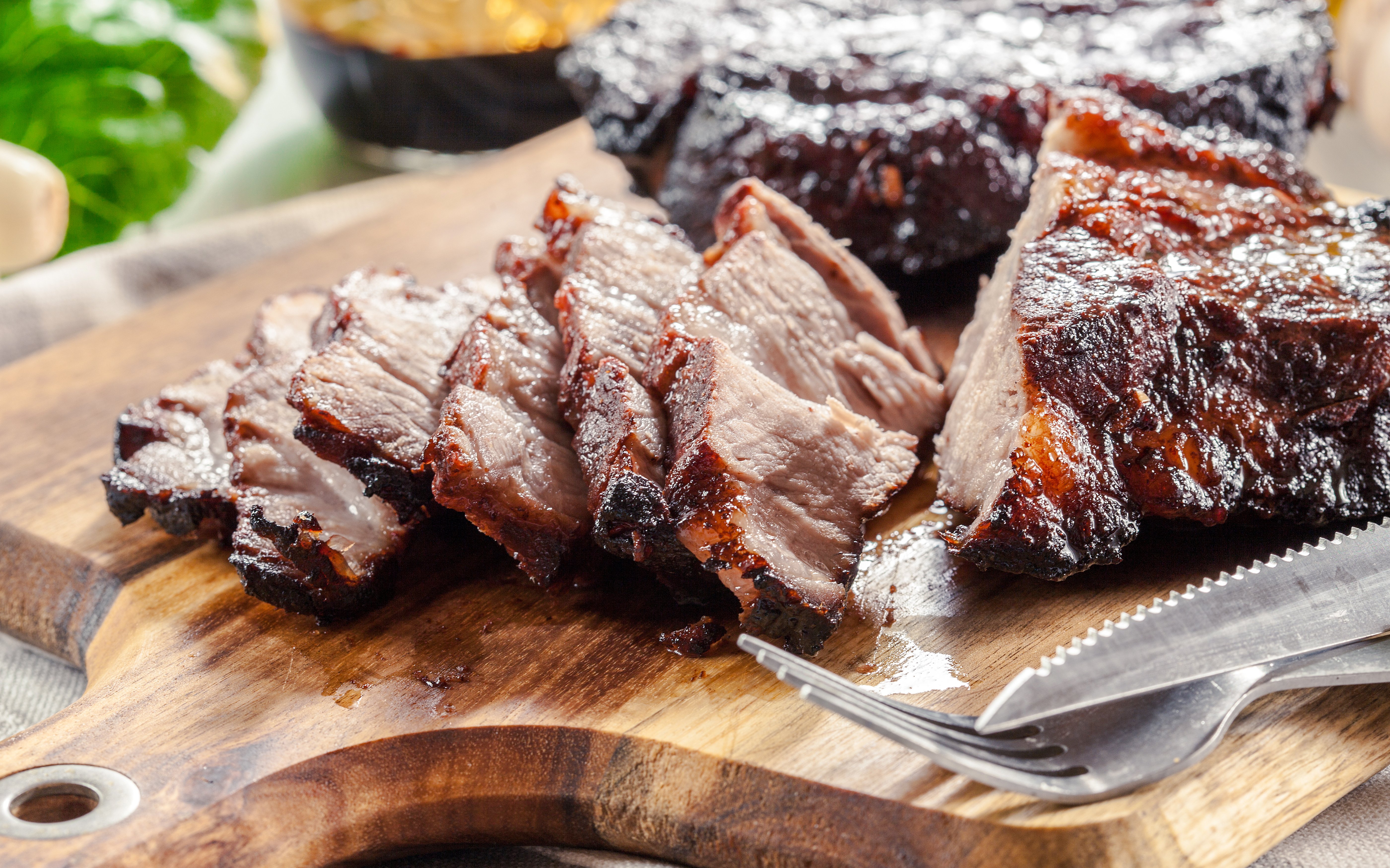 Sliced Char Siu Pork on a wooden board with a fork and knife.