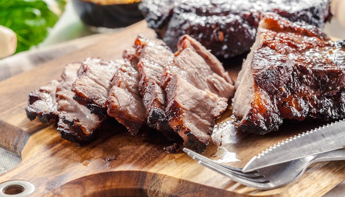 Sliced Char Siu Pork on a wooden board with a fork and knife.