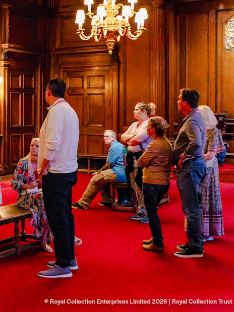 Tour group listening to a guide in the ornate gallery of the Palace of Holyroodhouse.