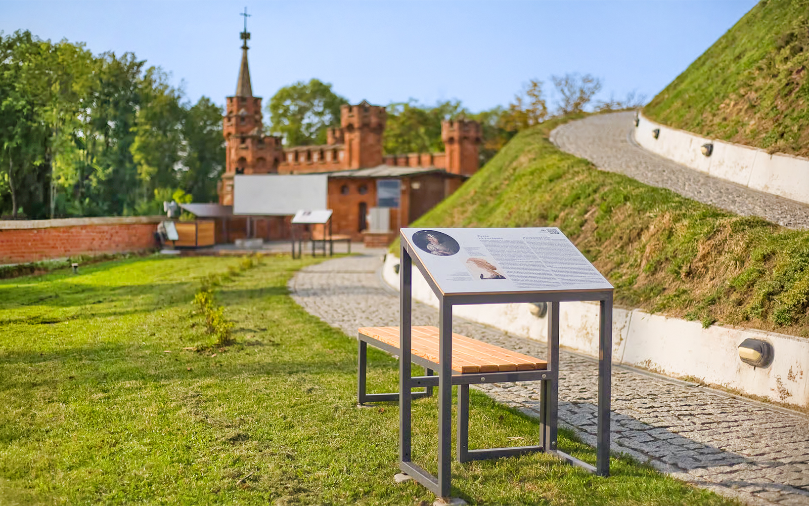 Interpretive sign and pathway at Kościuszko Mound, Krakow, with historic building in background.