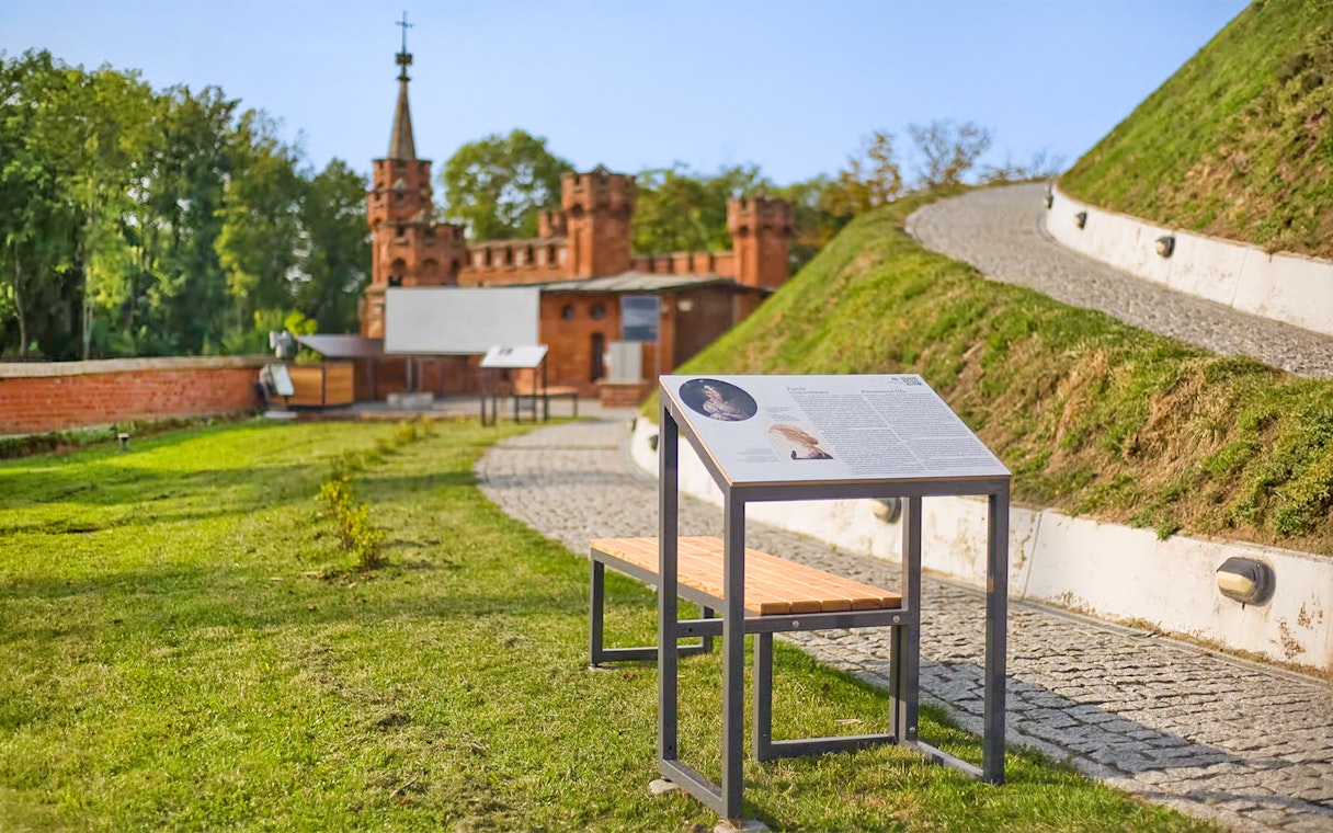 Interpretive sign and pathway at Kościuszko Mound, Krakow, with historic building in background.