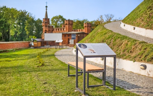 Interpretive sign and pathway at Kościuszko Mound, Krakow, with historic building in background.