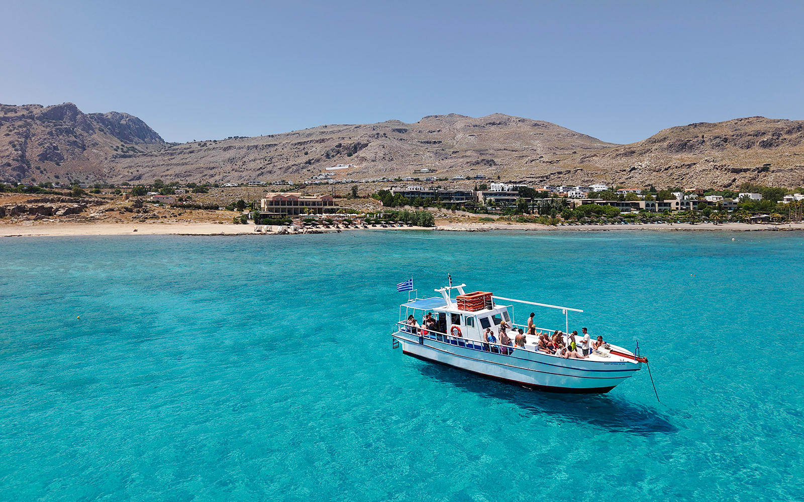 Boat cruising on turquoise waters near Lindos, Greece, with coastal landscape in the background.