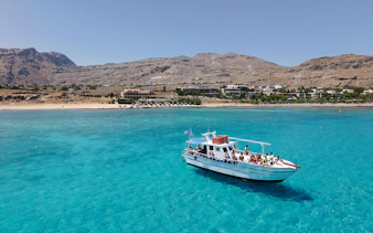 Boat cruising on turquoise waters near Lindos, Greece, with coastal landscape in the background.