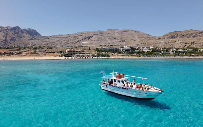 Boat cruising on turquoise waters near Lindos, Greece, with coastal landscape in the background.