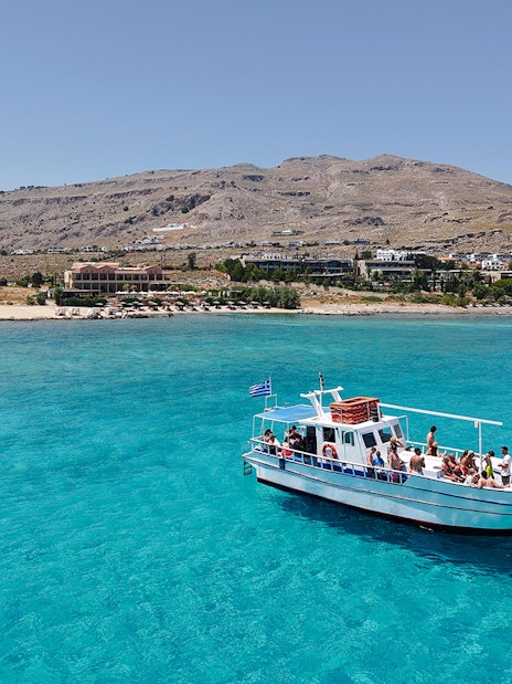 Boat cruising on turquoise waters near Lindos, Greece, with coastal landscape in the background.