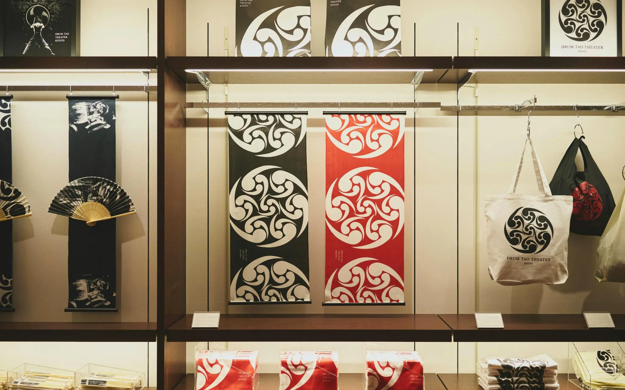Merchandise display at DRUM TAO Theater Kyoto featuring fans, banners, and tote bags.