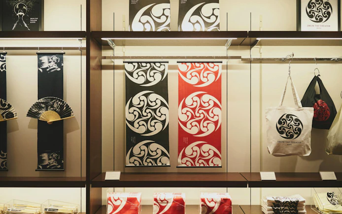Merchandise display at DRUM TAO Theater Kyoto featuring fans, banners, and tote bags.